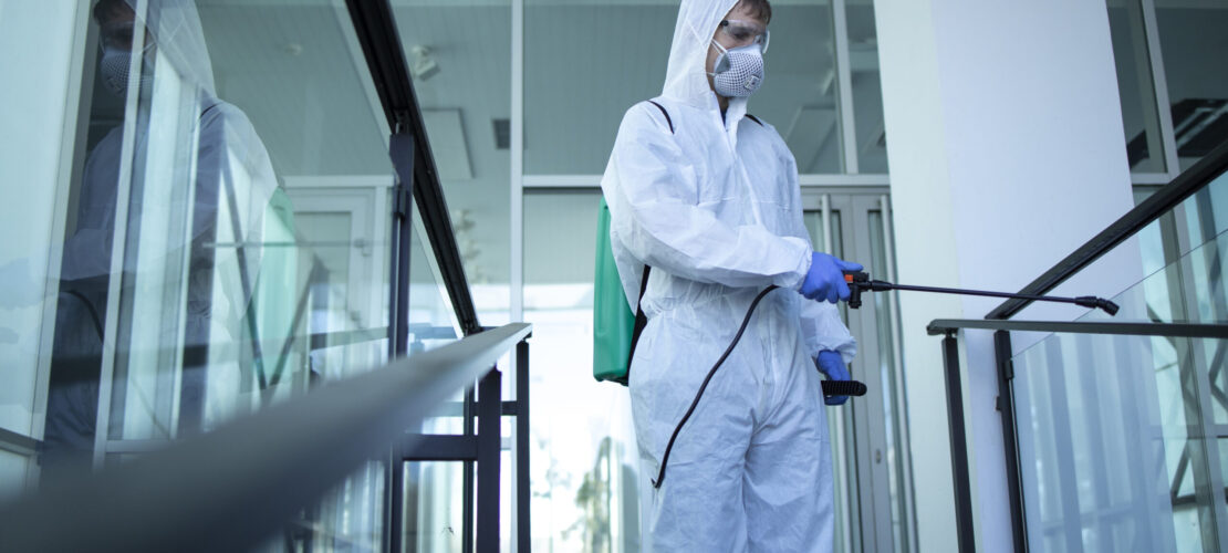 Unrecognizable person in white protection suit disinfecting public areas to stop spreading highly contagious corona virus.